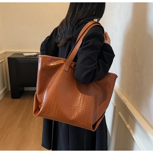 Detail of large brown crocodile embossed leather tote bag shown on a model side view