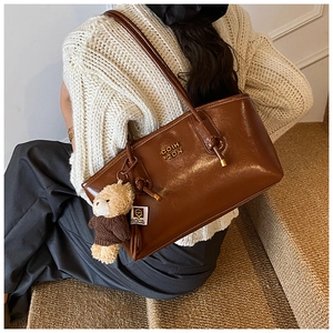 Detail of brown glossy leather tote bag featuring gold lettering and cute bear charm