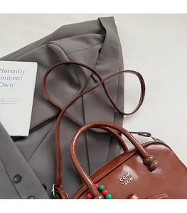 Close-up of brown patent leather pillow bag with round bead charms and crossbody strap