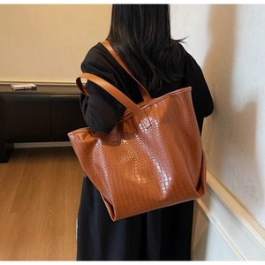 Detailed view of brown crocodile embossed leather tote bag shown on person for size