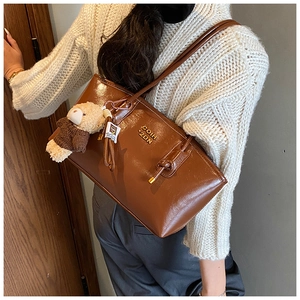 Detail of glossy brown tote bag with metal lettering and cute plush bear charm