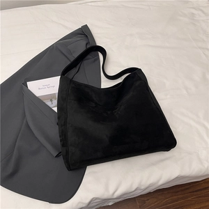 Dettaglio di una grande borsa tote nera opaca su un letto bianco con accessori