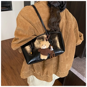 Detail view of glossy black faux leather tote bag with metal logo and plush bear charm