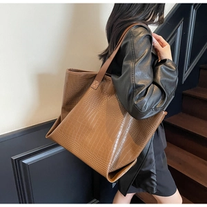 Detail shot of a dark brown crocodile embossed tote bag on a model in a minimalist setting