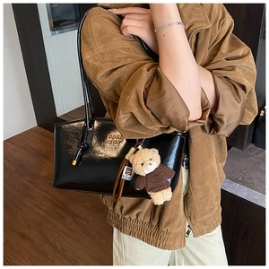 Detail of black glossy shoulder bag with slender straps and brown plush bear charm