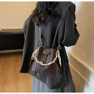 Close-up of brown woven bucket bag with silk scarf chain handle and crossbody strap