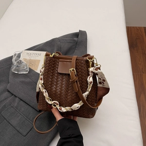 Detail of dark brown woven bucket bag with silk scarf chain and long strap on grey blazer