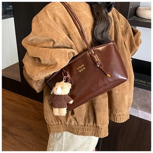 Brown patent leather tote bag with teddy bear pendant shown on model's shoulder