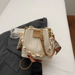 Detail of white woven bucket bag featuring floral scarf-wrapped chain handle and leather strap