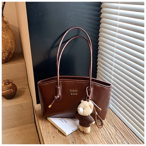 Detail of dark brown leather tote bag with gold logo and cute plush bear keychain
