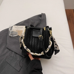 Detail of black woven bucket bag featuring gold hardware and silk scarf chain handle