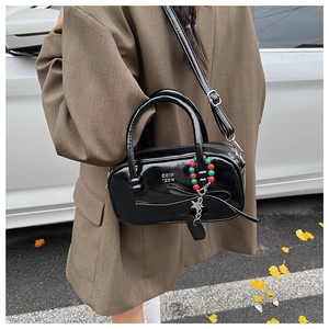 Detail of black patent leather bag featuring a side bow and beaded heart keychain