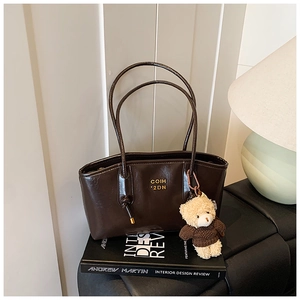 Detailed close-up of dark brown glossy leather tote bag with cute bear charm on books