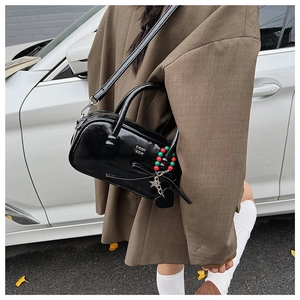 Detail of black patent leather pillow bag with bow and decorative charms held by model