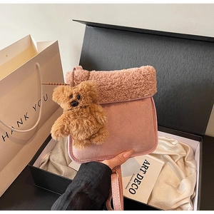 Detail of pink plush shoulder bag with teddy bear pendant on white satin background