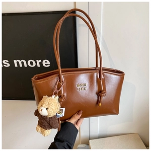 Close-up of brown glossy tote bag with gold logo and cute plush teddy bear charm detail