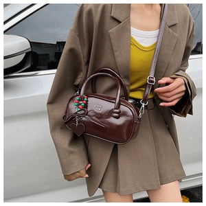 Detail of dark brown glossy leather Boston bag with metal logo and heart charm