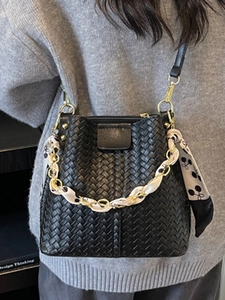 Fashionable black woven bucket bag with silk scarf chain handle worn by a model