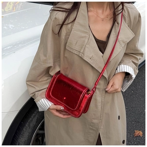 Dettaglio borsa a tracolla rossa metallizzata lucida con cuciture fini su un trench color kaki