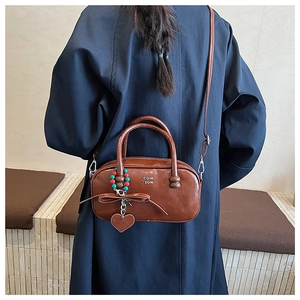 Detail view of brown glossy pillow bag with creative pendant and adjustable strap