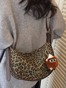 Leopard print crescent bag with plush charm, worn crossbody over grey knitwear