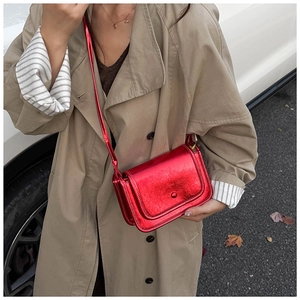 Scatto all'aperto di una borsa a tracolla rossa metallizzata lucida con patta elegante