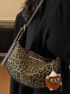 Leopard print crescent crossbody bag with plush charm on a black blazer model