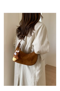 Detail of a brown suede crescent bag with a cute plush bear charm on a beige trench coat