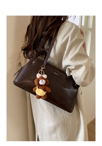 Detail of dark brown leather tote bag with a plush bear charm and brand logo plate
