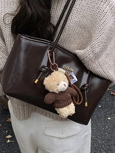 Vintage dark brown patent leather tote bag with bear charm in outdoor street style