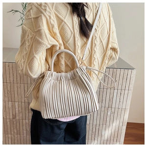 Detail of beige pleated cloud bag with rigid round handle and slim shoulder strap on model