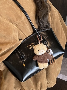 Glossy black tote bag with gold lettering and cute teddy bear pendant on model
