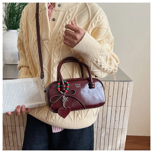 Close-up of wine red Boston bag with metal logo, beaded charms and detachable strap