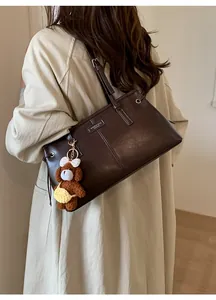 Deep brown leather shoulder bag with cute plush bear charm on a model in trench coat