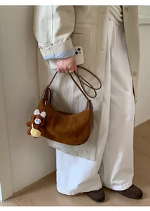 Detail of a brown suede half-moon shoulder bag with a cute plush bear charm accessory
