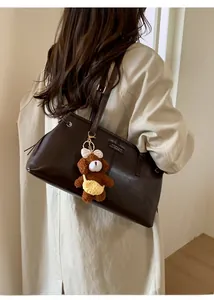 Detail view of deep brown matte leather tote bag with a cute plush bear charm