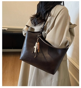 Detail of dark brown tote bag with vintage beaded charms on a beige trench coat