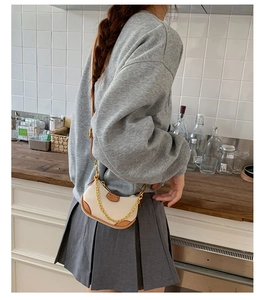 Détail d'un sac demi-lune crème minimaliste avec bordure en cuir marron et chaîne dorée