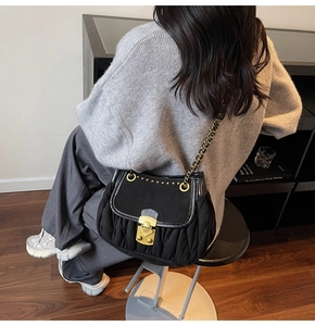 Close-up of black quilted shoulder bag with gold metal lock and rivet detailing