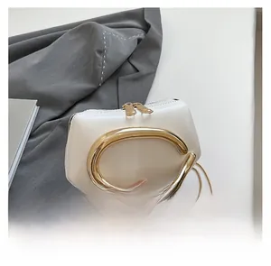 Detail of white mini box bag with large gold metal handle and chain strap on white desk