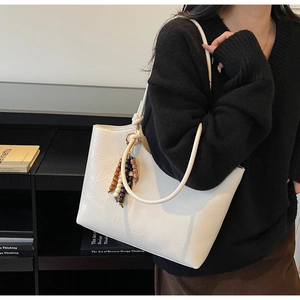 Close-up of a white leather tote bag with elegant beaded pendant and slim shoulder strap