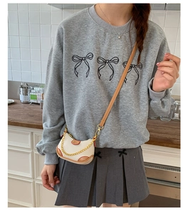 Détail d'un sweat gris avec motifs nœuds et sac à bandoulière blanc à chaîne métallique