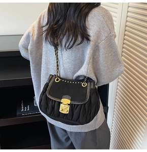 Detail of black matelassé shoulder bag with golden studs and chain strap on model