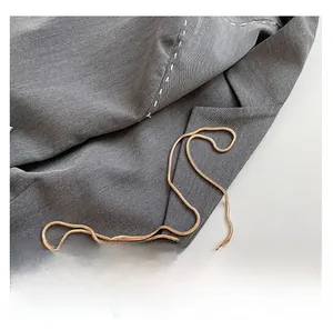 Detail of grey blazer fabric with white stitching and a sleek gold snake chain strap