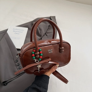Detail of dark brown glossy pillow bag with stylish charm and detachable strap