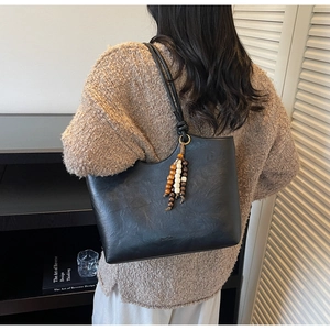 Detail of black faux leather tote with vintage pleated texture and wooden bead tassel