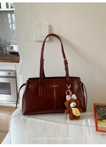 Detail of dark reddish-brown tote bag with plush bear charm on white sofa