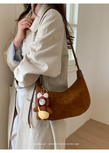 Detail of brown suede hobo bag with a cute bear charm on a trench coat shoulder
