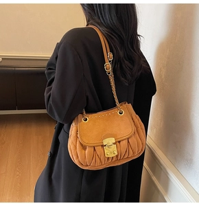 Close-up of brown suede ruched shoulder bag with gold hardware worn by a model