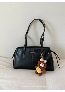 Detail of minimalist black leather underarm bag with a cute brown plush bear charm accessory